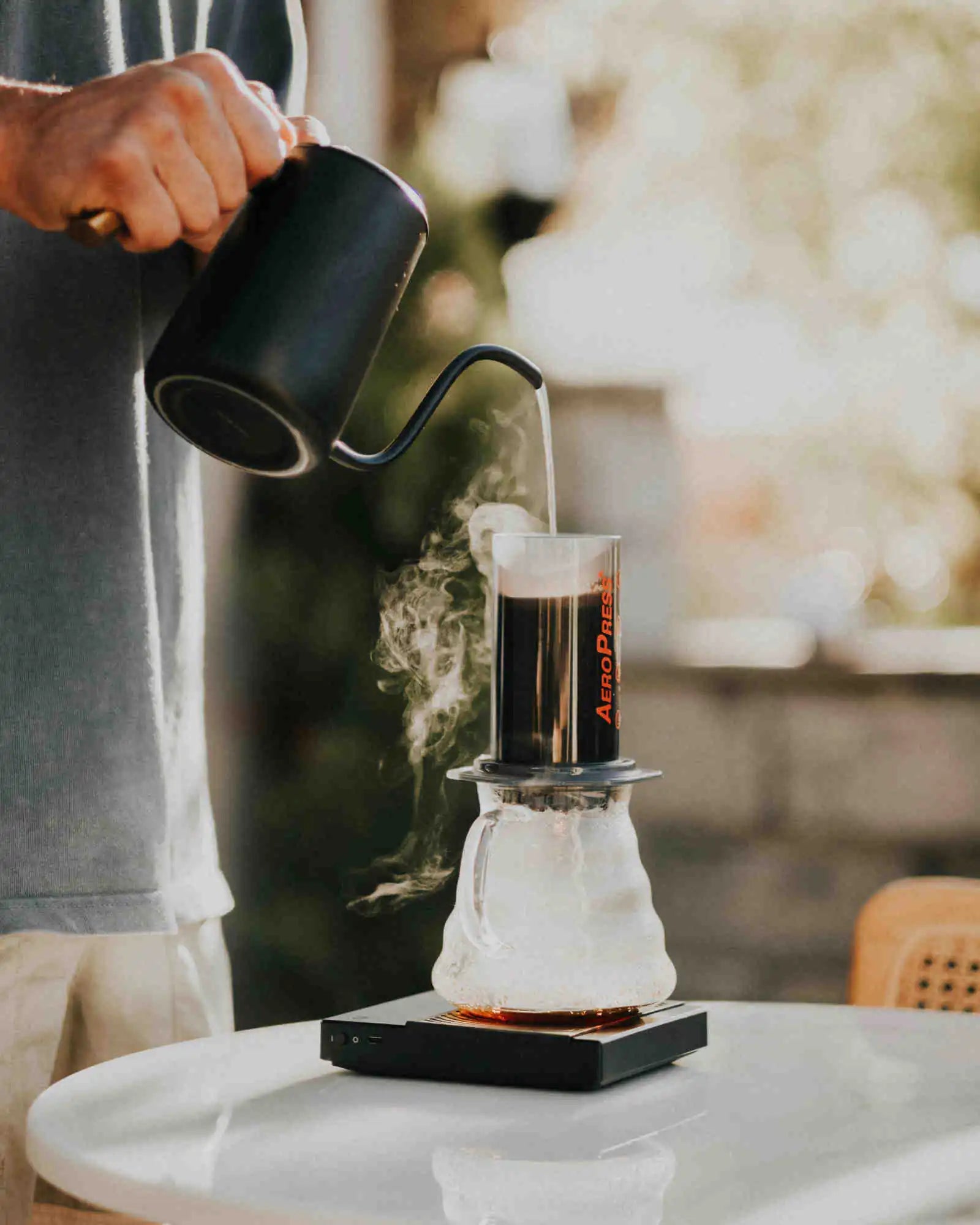 Person pouring coffee into an AeroPress on a table with a blurred background
