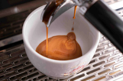 Espresso being poured into a white cup on a metal surface