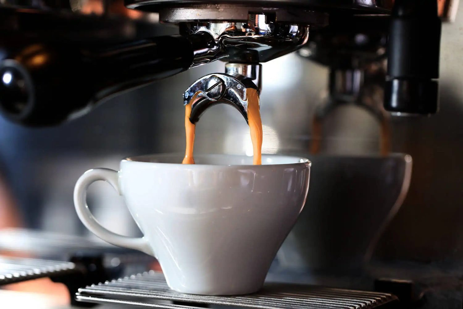 Espresso being poured into a white cup from an espresso machine.